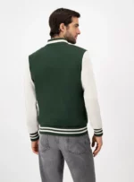 Hombre de espaldas usando chamarra beisbolera color verde y blanco.