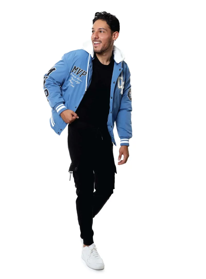 Hombre con chamarra beisbolera azul, pantalones negros y tenis blancos