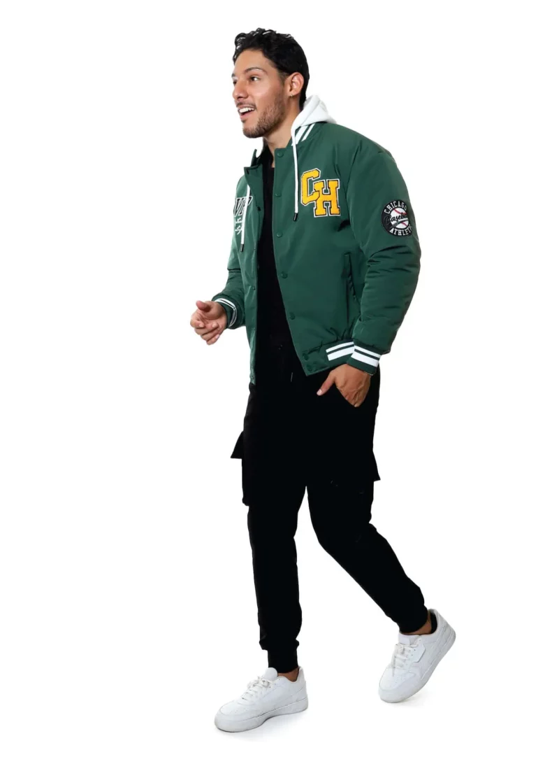 Hombre con chamarra beisbolera verde, pantalones negros y tenis blancos