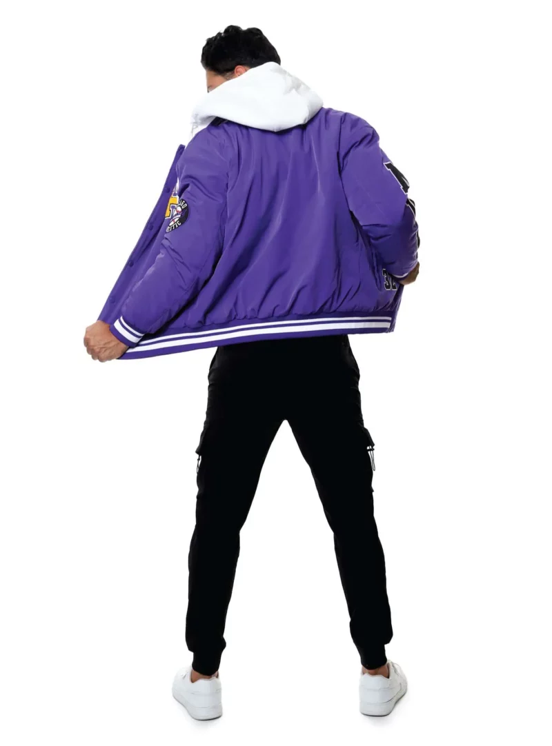 Hombre con chamarra beisbolera color morado y pantalones negros con tenis blancos.